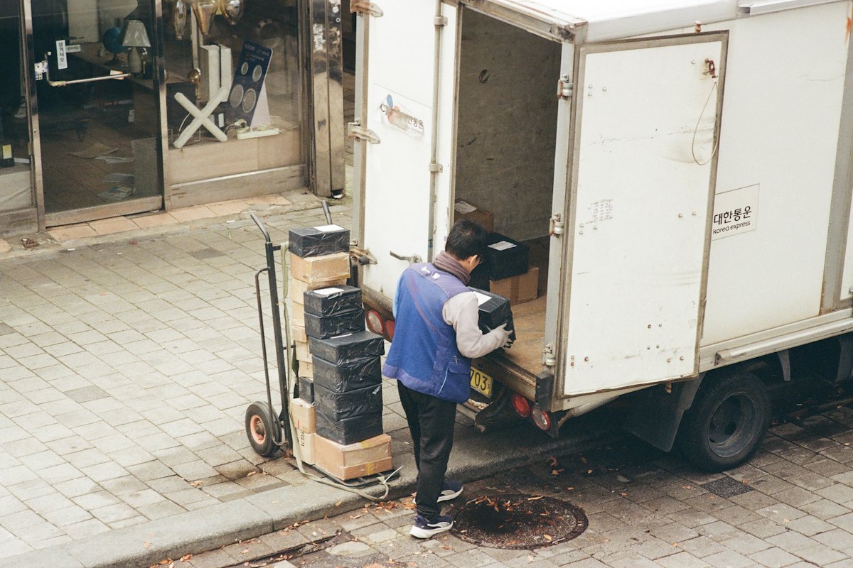 Repartidor descargando cajas de un camión con una carretilla a la puerta de un negocio